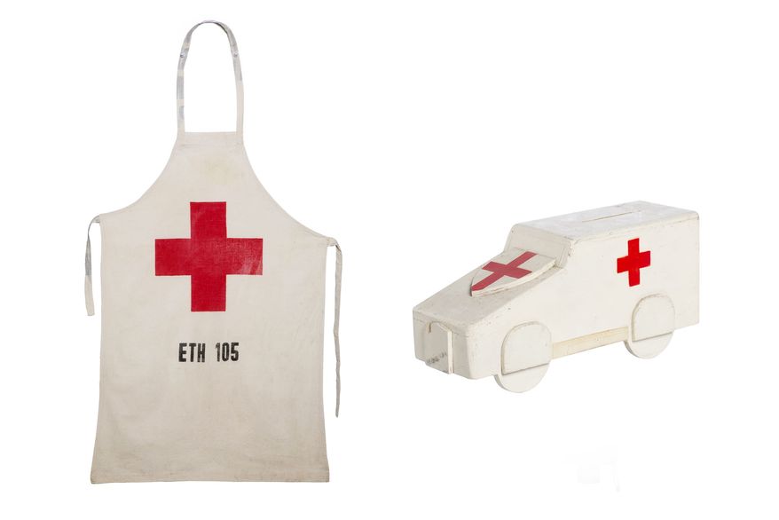Red Cross apron made from a flour sack 1984 & Wooden British Red Cross collecting box in the shape of an ambulance Circa 1920s | collection photography | © British Red Cross Museum & Archives